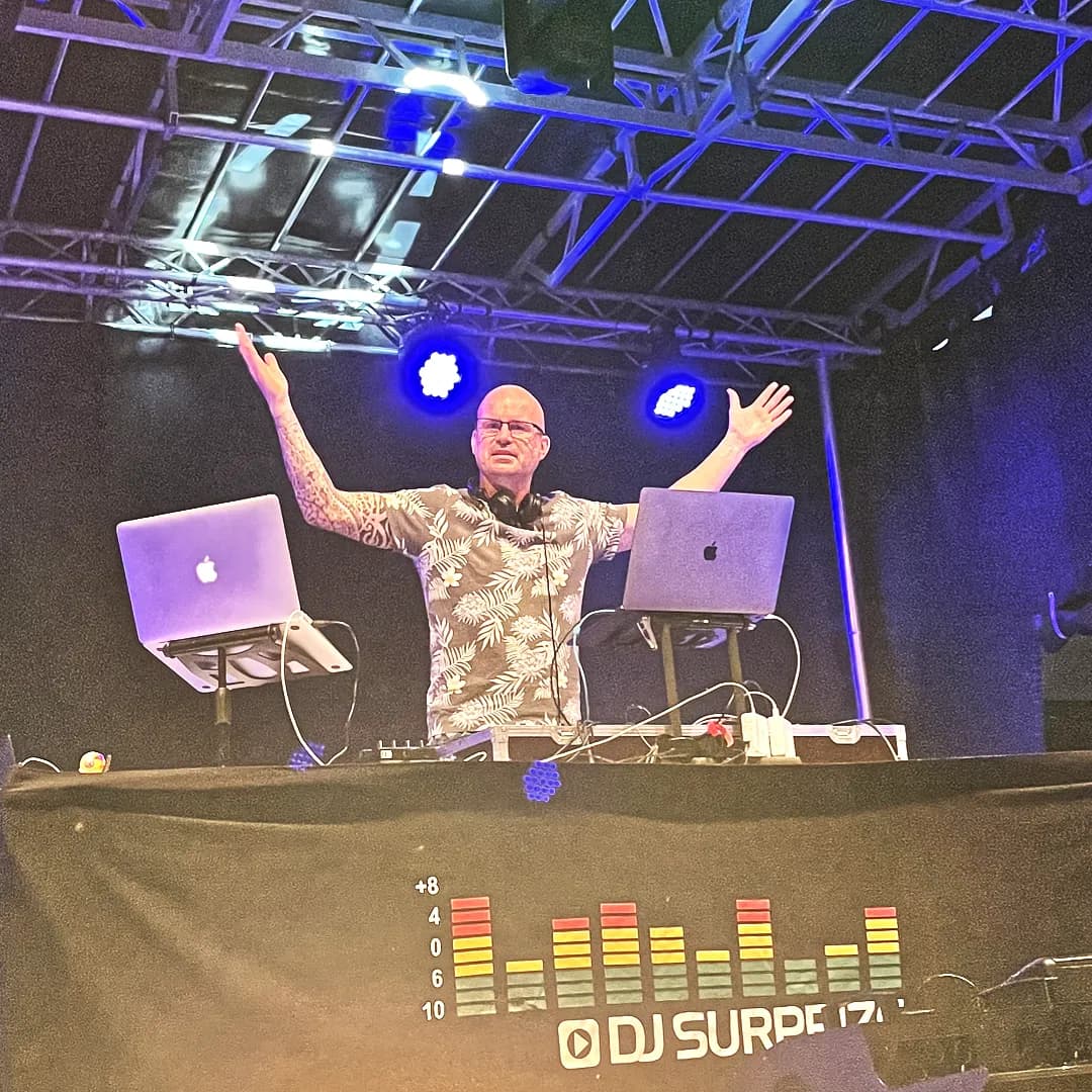 DJ beim Auflegen an zwei Laptops auf einer Bühne, blaue Scheinwerfer und Trussing im Hintergrund