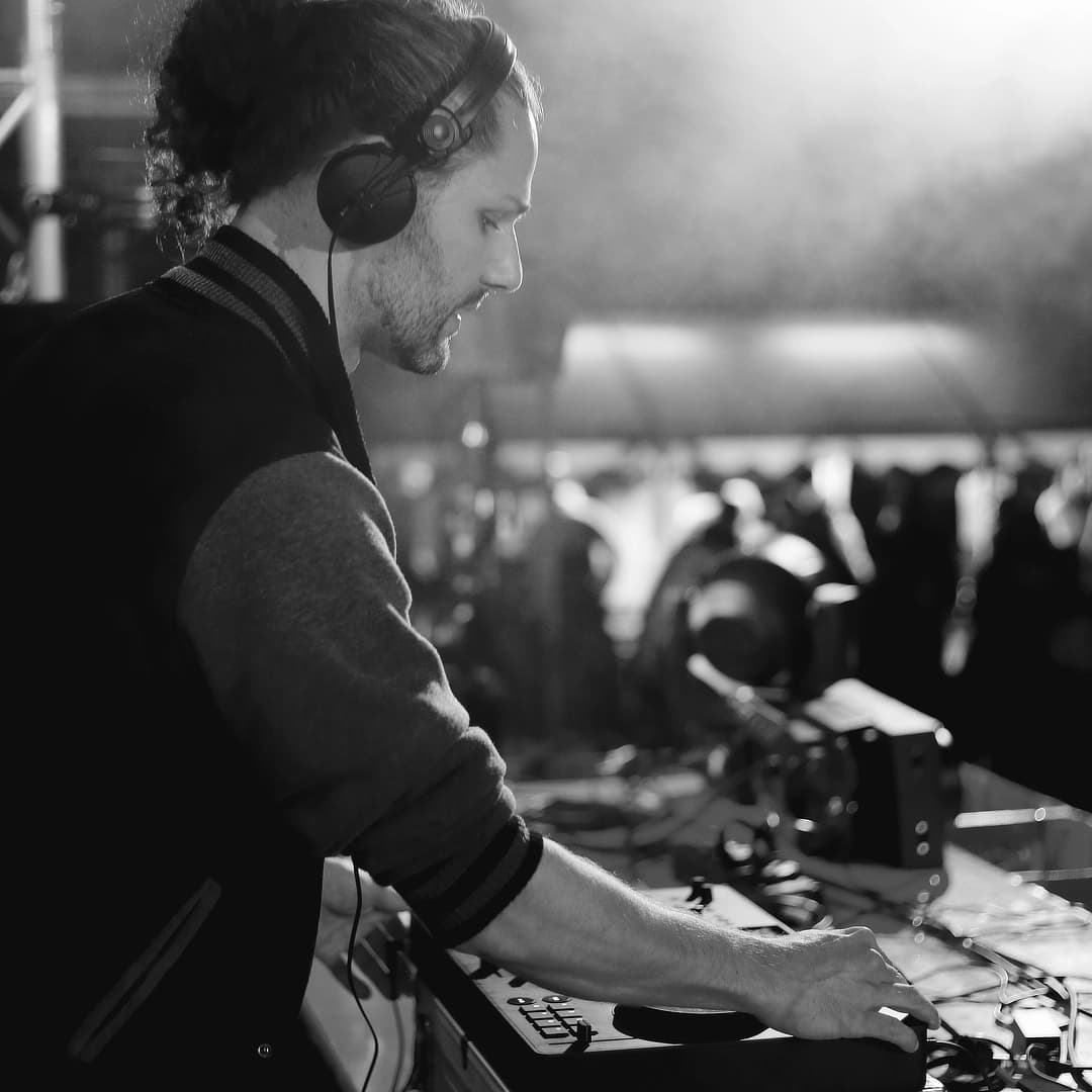 DJ mit Kopfhörern konzentriert am Mischpult, Schwarzweiß-Aufnahme von der Seite